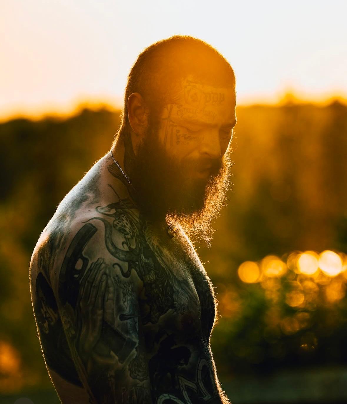 A person with a beard and tattoos

Description automatically generated